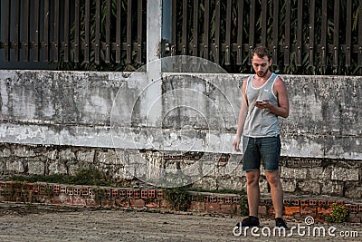 Young guy in a gray tank top and jeans shorts smokes Stock Photo