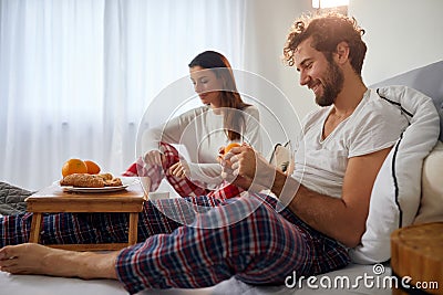 A young guy with his girlfriend in the bed peeling off an orange for a breakfast. Love, relationship, together Stock Photo