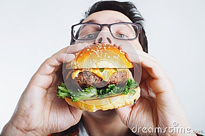 A young guy is holding a fresh Burger. A very hungry student eats fast food. Hot helpful food. The concept of gluttony and unhealt Stock Photo