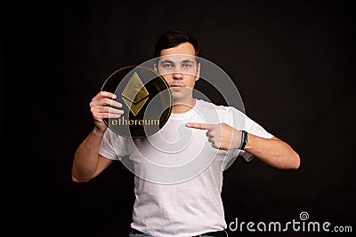 A young guy holds a symbol of the ethereum coin, a modern currency for exchange and purchases Editorial Stock Photo