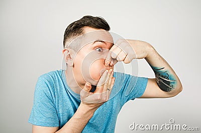 Young guy inserts two fingers in the mouth to induce vomiting, on a light background Stock Photo