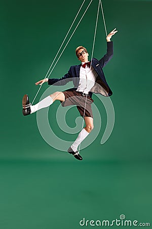 Young guy, marionette on string in motion against green studio background. Puppet. Pressure and manipulation Stock Photo