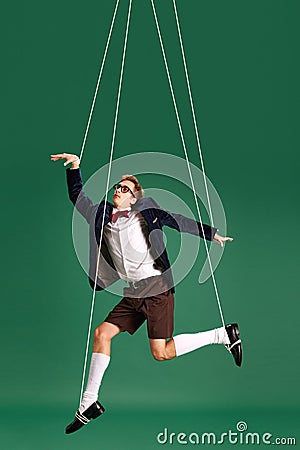 Young guy, marionette on string in motion against green studio background. Puppet. Pressure and manipulation Stock Photo