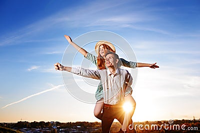 Young guy piggybacking cheerful girlfriend like airplane on the background of sky Stock Photo