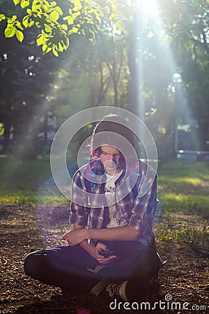 Young guy with purple hair sitting on a skateboard in the park Stock Photo