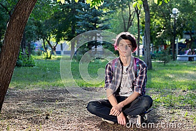 Young guy with purple hair sitting on a skateboard in the park Stock Photo