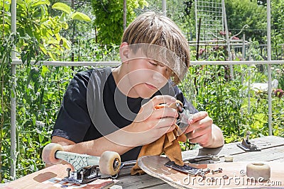 Young guy repairs the wheels on a skateboard on a wooden stall in the garden Stock Photo