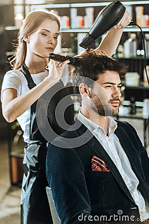 Young hairstylist combing and drying hair to handsome client Stock Photo