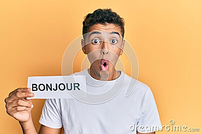 Young handsome african american man holding bonjour french greeting word scared and amazed with open mouth for surprise, disbelief Stock Photo