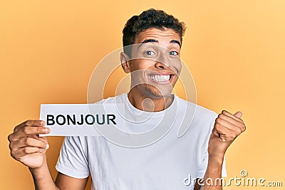 Young handsome african american man holding bonjour french greeting word screaming proud, celebrating victory and success very Stock Photo