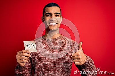 Young handsome african american man holding reminder paper with yes message happy with big smile doing ok sign, thumb up with Stock Photo