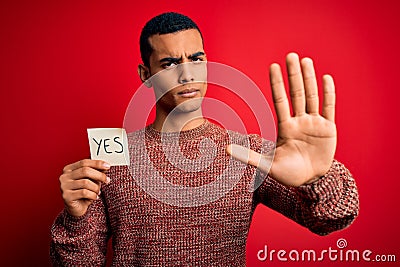 Young handsome african american man holding reminder paper with yes message with open hand doing stop sign with serious and Stock Photo