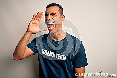 Young handsome african american man volunteering wearing t-shirt with volunteer message shouting and screaming loud to side with Stock Photo