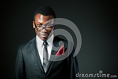 Young handsome african businessman in grey costume, white shirt, tie and glasses standing and smiling Stock Photo