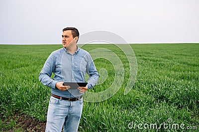 Young handsome agronomist, agriculture engineer standing in green wheat field with tablet in hands in early summer. Agribusiness Stock Photo