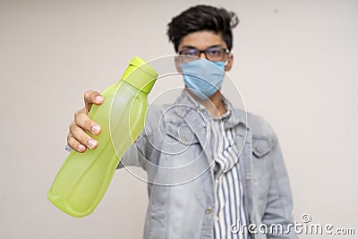 Young handsome asian boy in denims, wearing a protective mask, holding a water bottle. Confident boy showing to drink more water Stock Photo