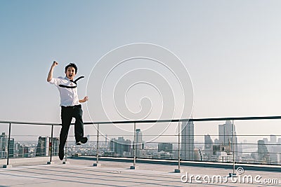 Young handsome Asian businessman jumping celebrate success winning pose on building roof. Work, job, or success concept Stock Photo