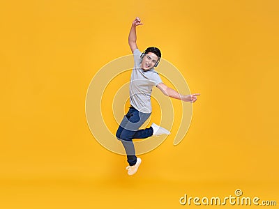 Young handsome Asian man smiling and jumping wearing wireless headphone listening to music isolated over yellow background Stock Photo