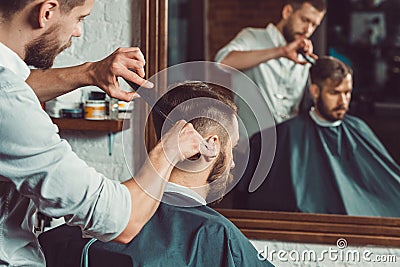 Young handsome barber making haircut of attractive man in barbershop Stock Photo