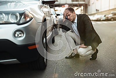 Young handsome businessman checking wheel of his car having problems on the road , unexpectable vehicle trouble Stock Photo