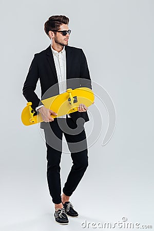 Young handsome businessman in suit and suglasses holding yellow skateboard Stock Photo