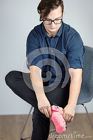 Young handsome caucasian male with dark curly hair pulls on bright pink sock with piglet. Stock Photo