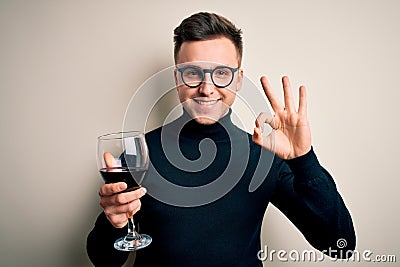 Young handsome caucasian man drinking an alcoholic glass of red wine over isolated background doing ok sign with fingers, Stock Photo
