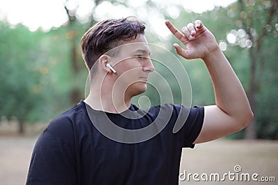 Young handsome caucasian man stands liftiing his hand up with pointed finger, at the middle of park or forest. Slightly smiling, w Stock Photo