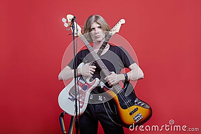 Young handsome caucasian man stands with two guitar, acoustic and electric ones in front of the stack with microphone. Musician po Stock Photo