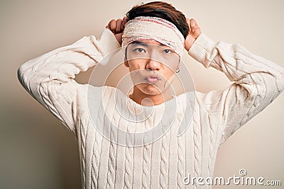 Young handsome chinese man injured for accident wearing bandage and strips on head doing funny gesture with finger over head as Stock Photo