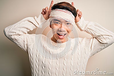 Young handsome chinese man injured for accident wearing bandage and strips on head Posing funny and crazy with fingers on head as Stock Photo