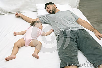 Young handsome father tired sleeping withone year baby girl. Bearded dad sleeps with baby in bed. Little newborn child in white Stock Photo