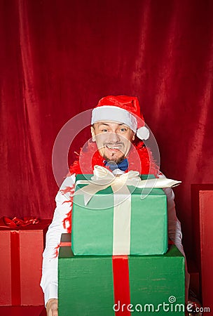 Young handsome funny man wearing Santa hat holding heavy Christmas gift boxes on the red background Stock Photo