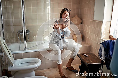 A young handsome girl in a bathroom at home talking on the phone while preparing for a work. Bathroom, morning, preparation Stock Photo