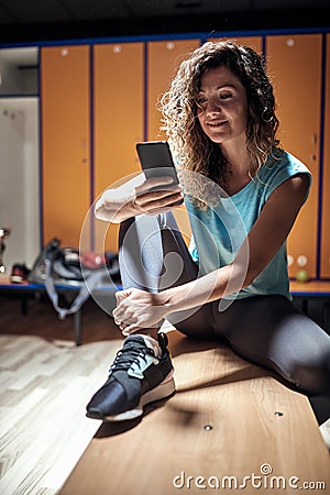 A young handsome girl texting on smartphone while waiting for a fitness training. Recreation, fitness and sport Stock Photo
