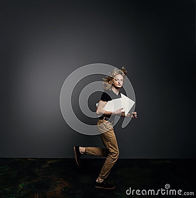 Young handsome guy in a black T-shirt with long blonde hair runs briskly holding an arrow in his hands on a gray background Stock Photo