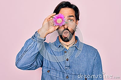 Young handsome hispanic bohemian hipster man with bear holding real pink flower scared in shock with a surprise face, afraid and Stock Photo