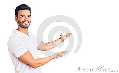 Young handsome hispanic man wearing casual clothes inviting to enter smiling natural with open hand Stock Photo