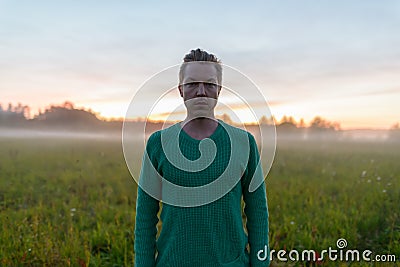 Young handsome man against grass field with fog in the break of dawn Stock Photo