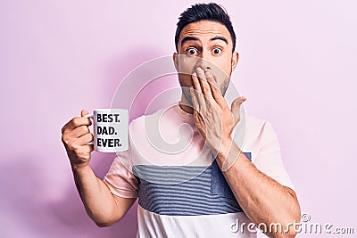 Young handsome man with beard drinking mug of coffee with best dad ever message covering mouth with hand, shocked and afraid for Stock Photo