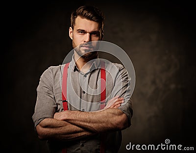 Young handsome man with beard wearing suspenders and posing on dark background. Stock Photo