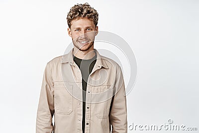 Young handsome man with curly stylish haircut, smiling at camera and looking happy, standing in autumn clothes, white Stock Photo