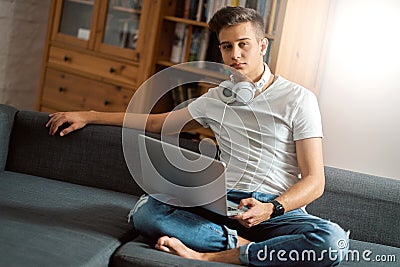 Young handsome man with laptop on gray sofa at home Stock Photo