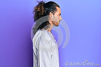 Young handsome man with long hair wearing bohemian and hippie shirt looking to side, relax profile pose with natural face with Stock Photo