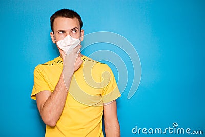 Young handsome man in medical mask and yellow t-shirt think how to dispose of problem isolated on blue background. Makes up an Stock Photo
