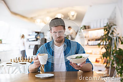 Young handsome man seems to be unhappy with with quality of salad and taste of coffee during lunch at the cafe, complaints and Stock Photo