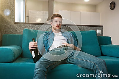 Young handsome man sitting on the sofa with a bottle of wine drinking in the cozy living room home relaxed atmosphere Stock Photo