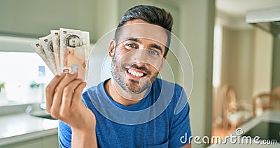 Young handsome man smiling happy holding england pounds banknotes at home Editorial Stock Photo