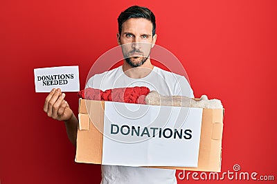 Young handsome man volunteer holding box and donations needed paper relaxed with serious expression on face Stock Photo