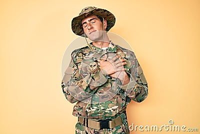 Young handsome man wearing camouflage army uniform smiling with hands on chest with closed eyes and grateful gesture on face Stock Photo